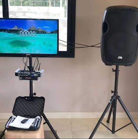 Kit de karaokê com TV, caixa no tripé, aparelho e maleta de microfones.